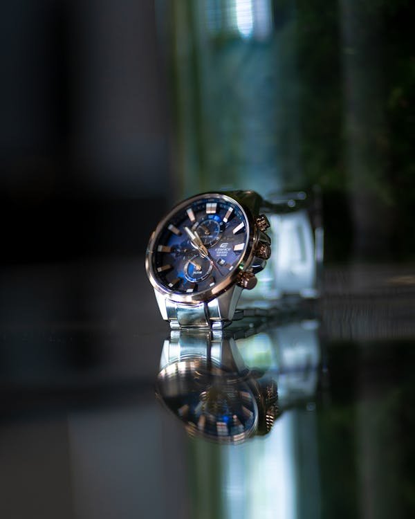 Elegant silver wristwatch with striking blue dial reflecting on a glass surface.
