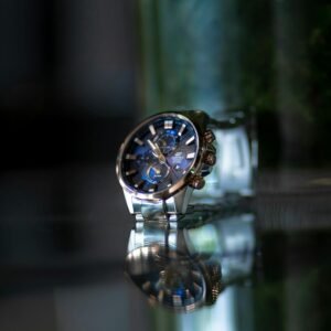 Elegant silver wristwatch with striking blue dial reflecting on a glass surface.