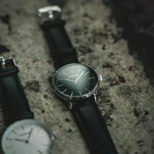 Stylish analog wristwatches with black leather straps displayed on a textured stone background.